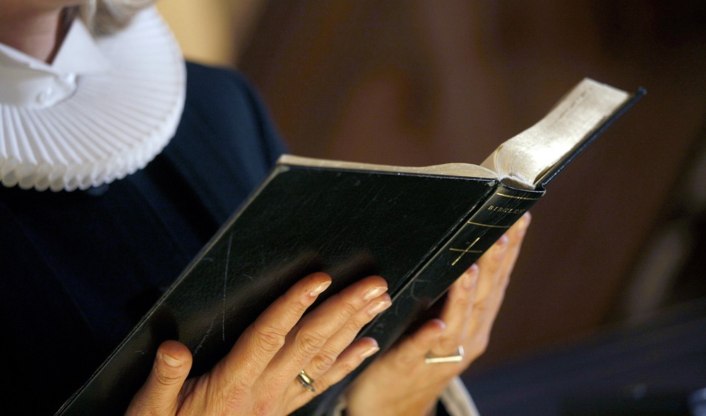 Præst i præstekjole holder opslået Bibel i hænderne